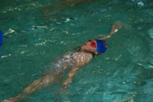 girl-swmming-on-her-back-in-a-blue-swim-cap-and-goggles-at-flow-aquatics-swim-school